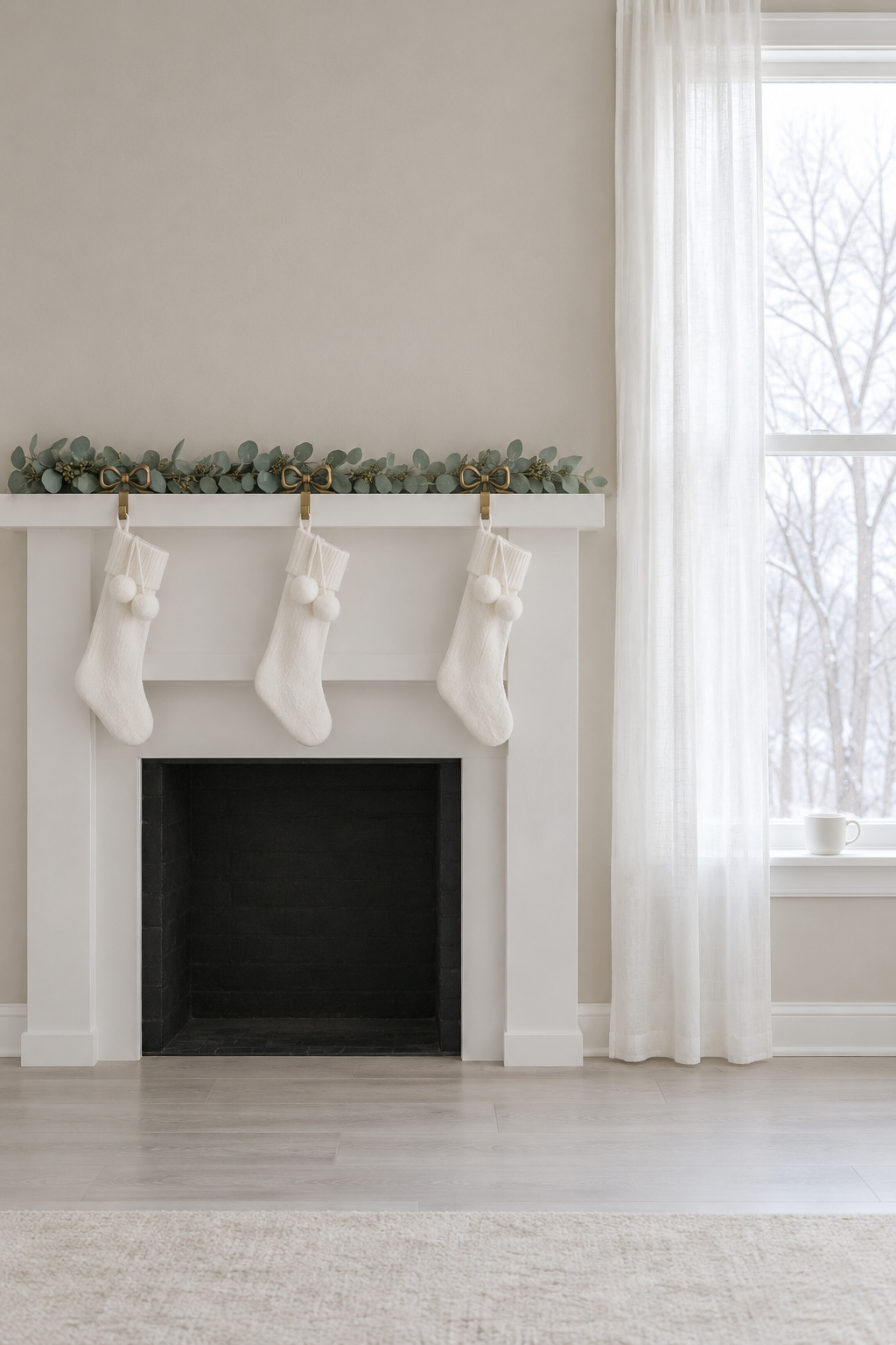 Pale Christmas mantle with a seeded eucalyptus garland lying along a white mantel and three white knit stockings with pom poms on brass bow stocking holders