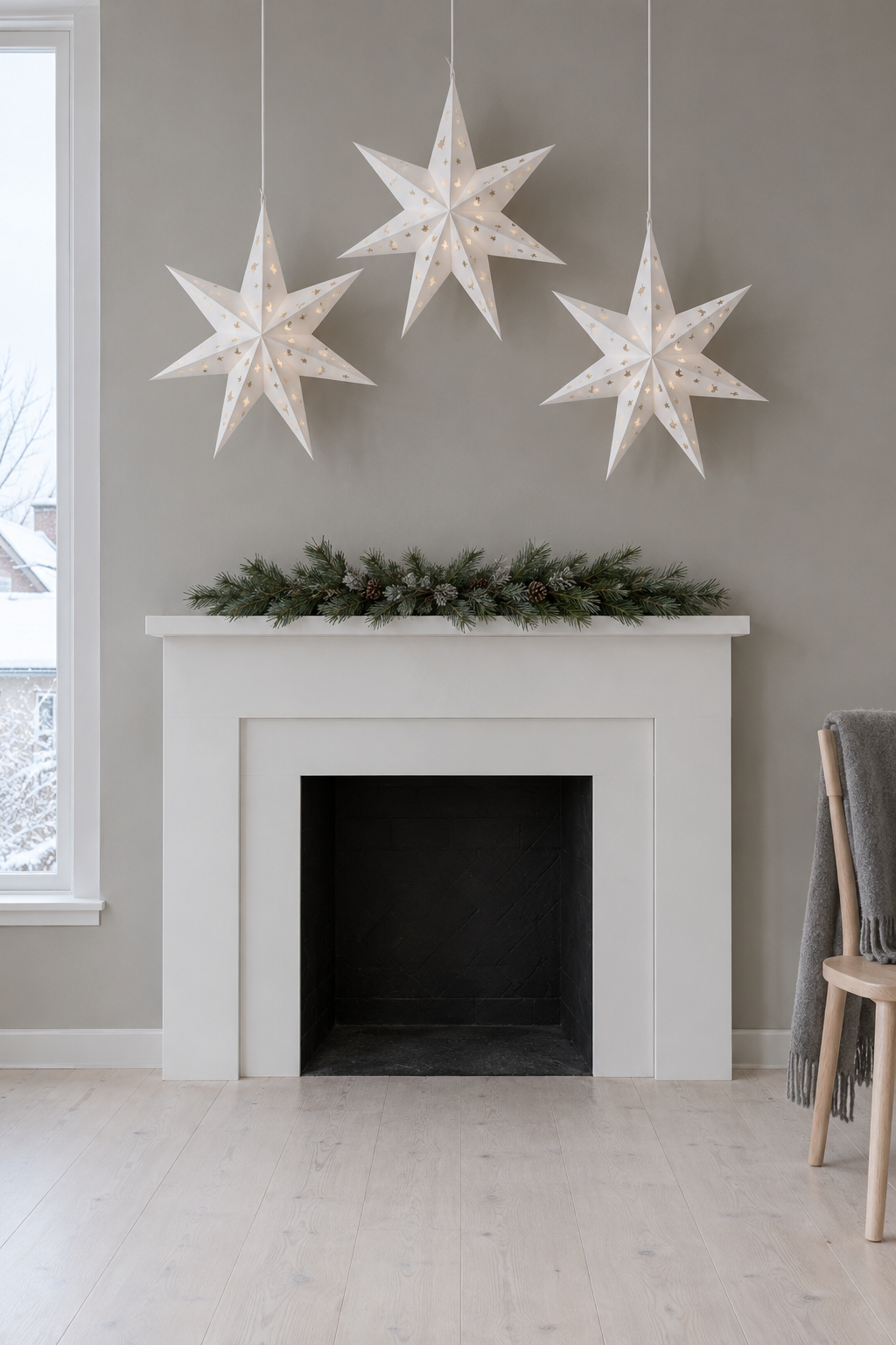 Scandinavian Christmas mantle with three white seven-pointed paper stars hung at different heights on the wall above a white mantel and one low pine swag on the shelf